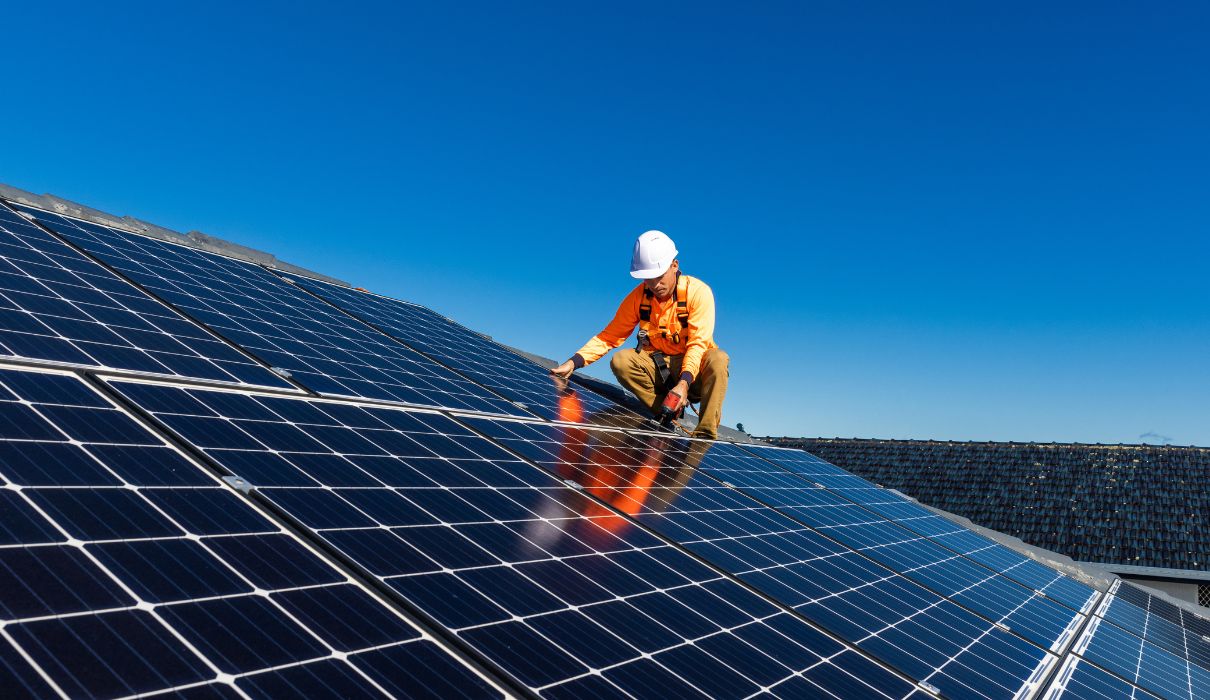 Top Solar Asia installer in orange high-visibility clothing fitting panels on a residential roof under a clear blue sky